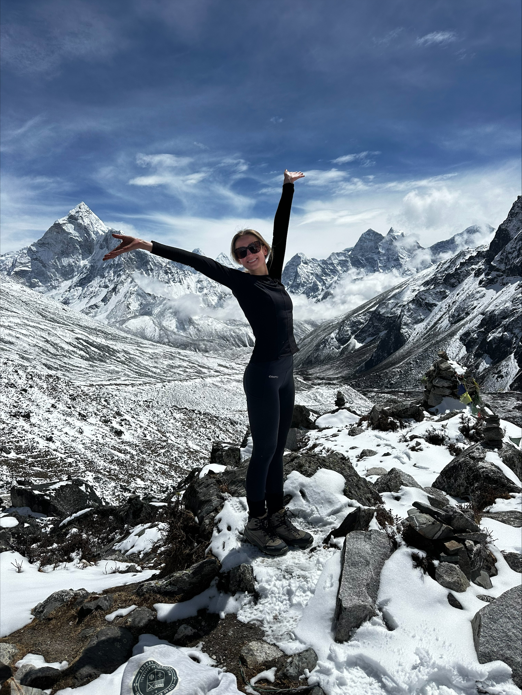 Vrolijke hiker staat met de armen wijd op een besneeuwde rots in de Himalaya met imposante bergtoppen op de achtergrond.