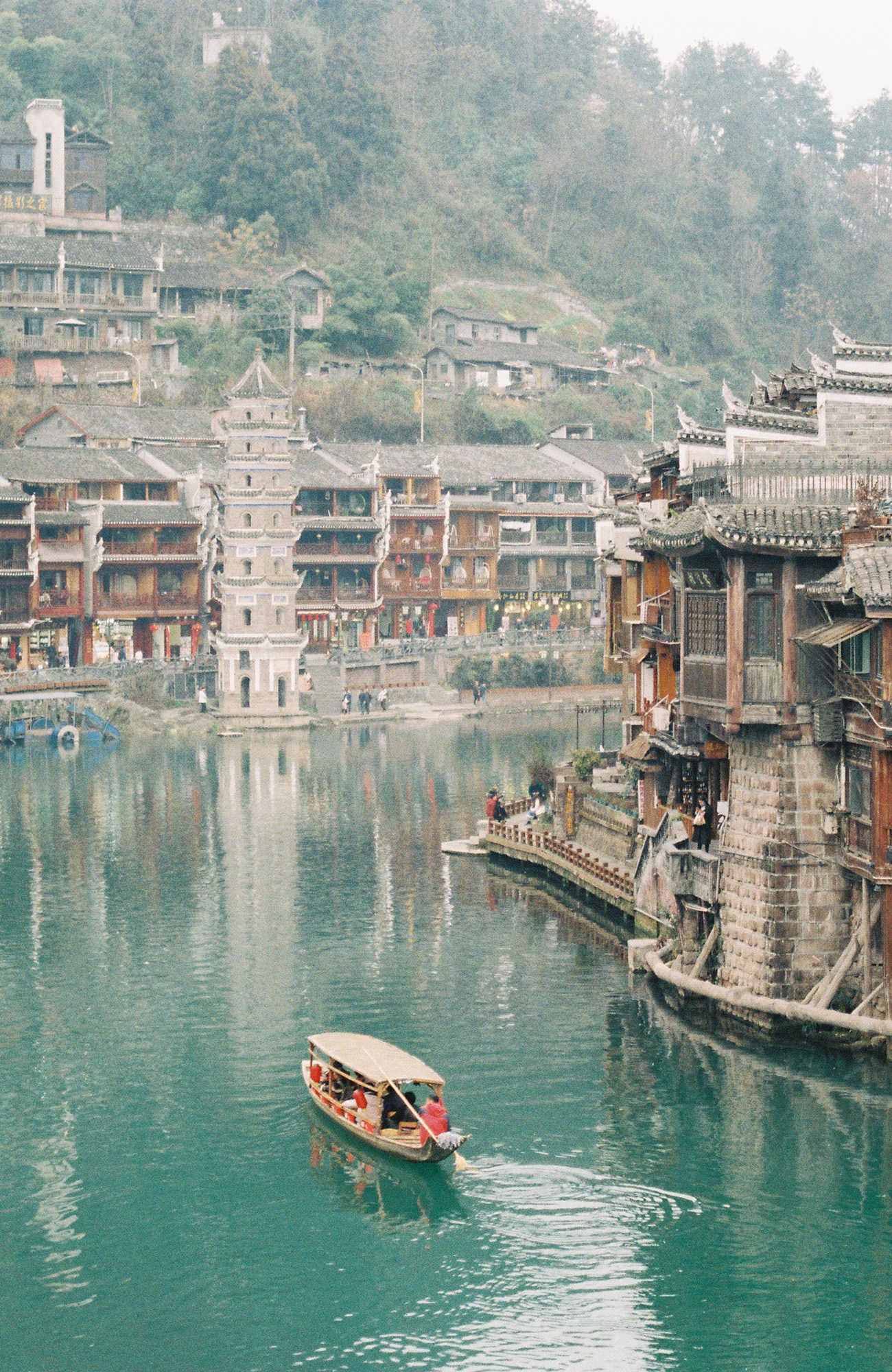 Boot vaart over een rivier langs een dorp | Rondreis China | KILROY