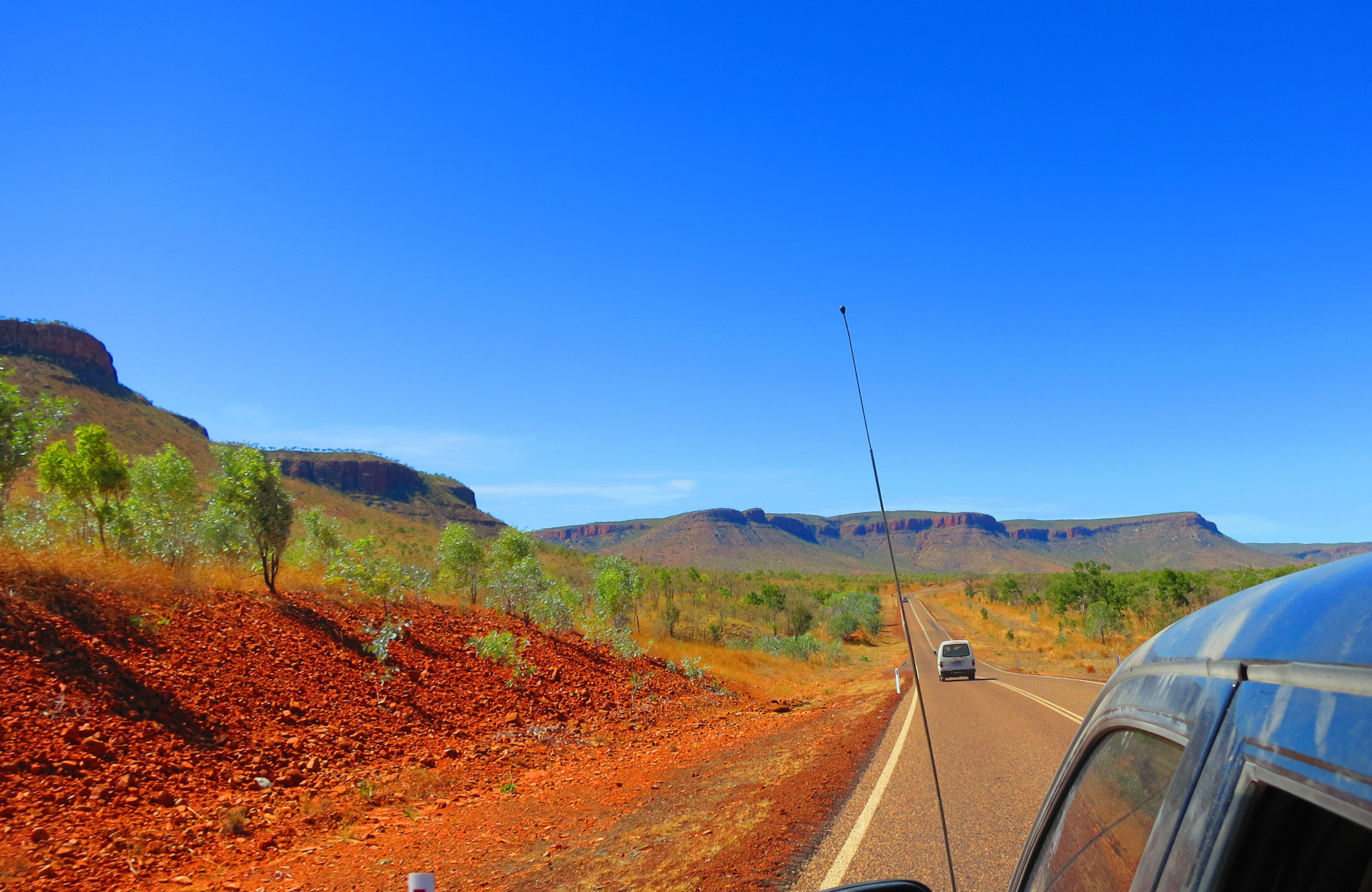 Een auto rijd door de Australische outback, je ziet de weg tussen de bergen en bomen