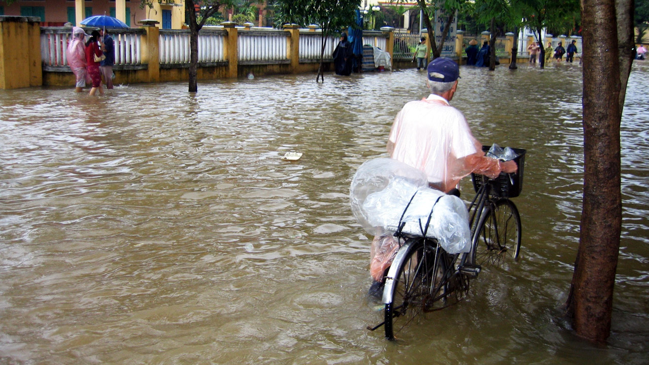 Man loopt met zijn fiets door een straat die ondergelopen is met water in Azië 