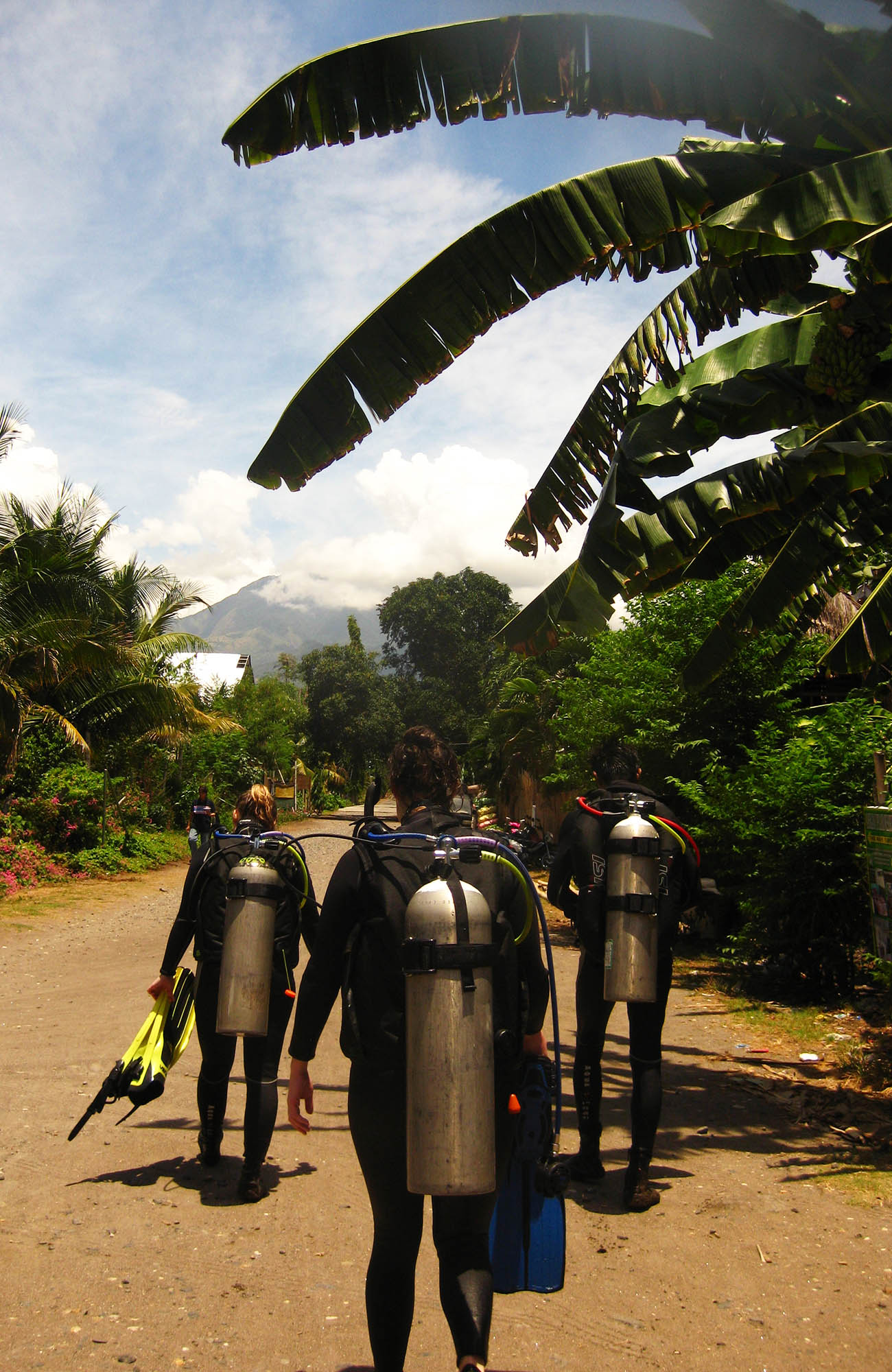 Divers walking with air tanks on their backs back from the ocean to the camp location