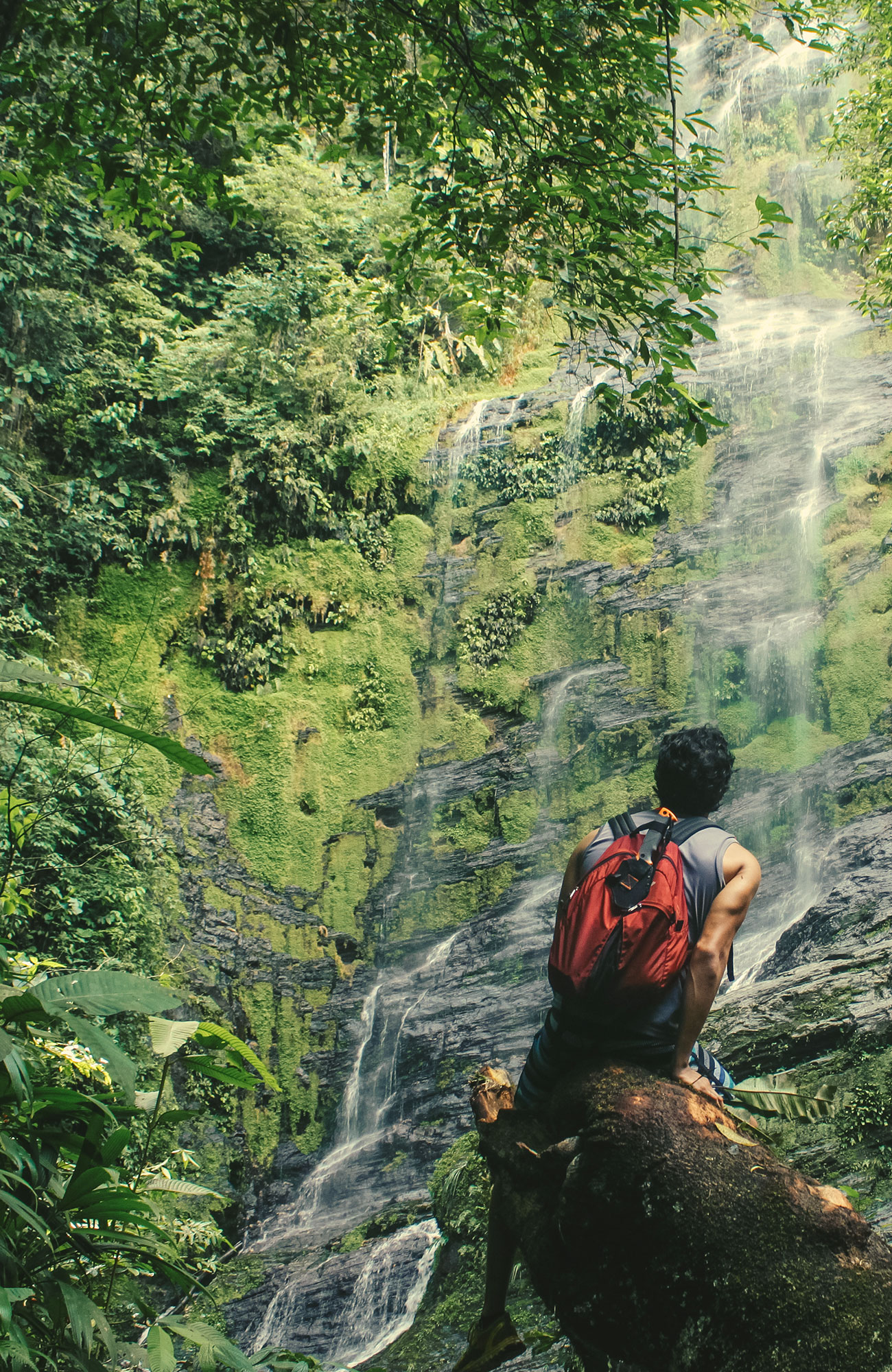Backpacker sitting on a tree log in front of a waterfall in Costa Rica