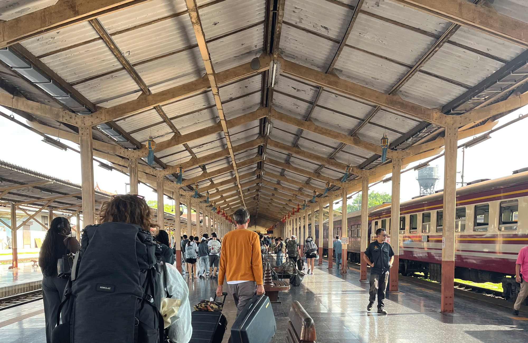 Reizigers met rugzakken en koffers staan te wachten op het perron van het treinstation in Bangkok, klaar voor de nachtelijke reis naar Chiang Mai.