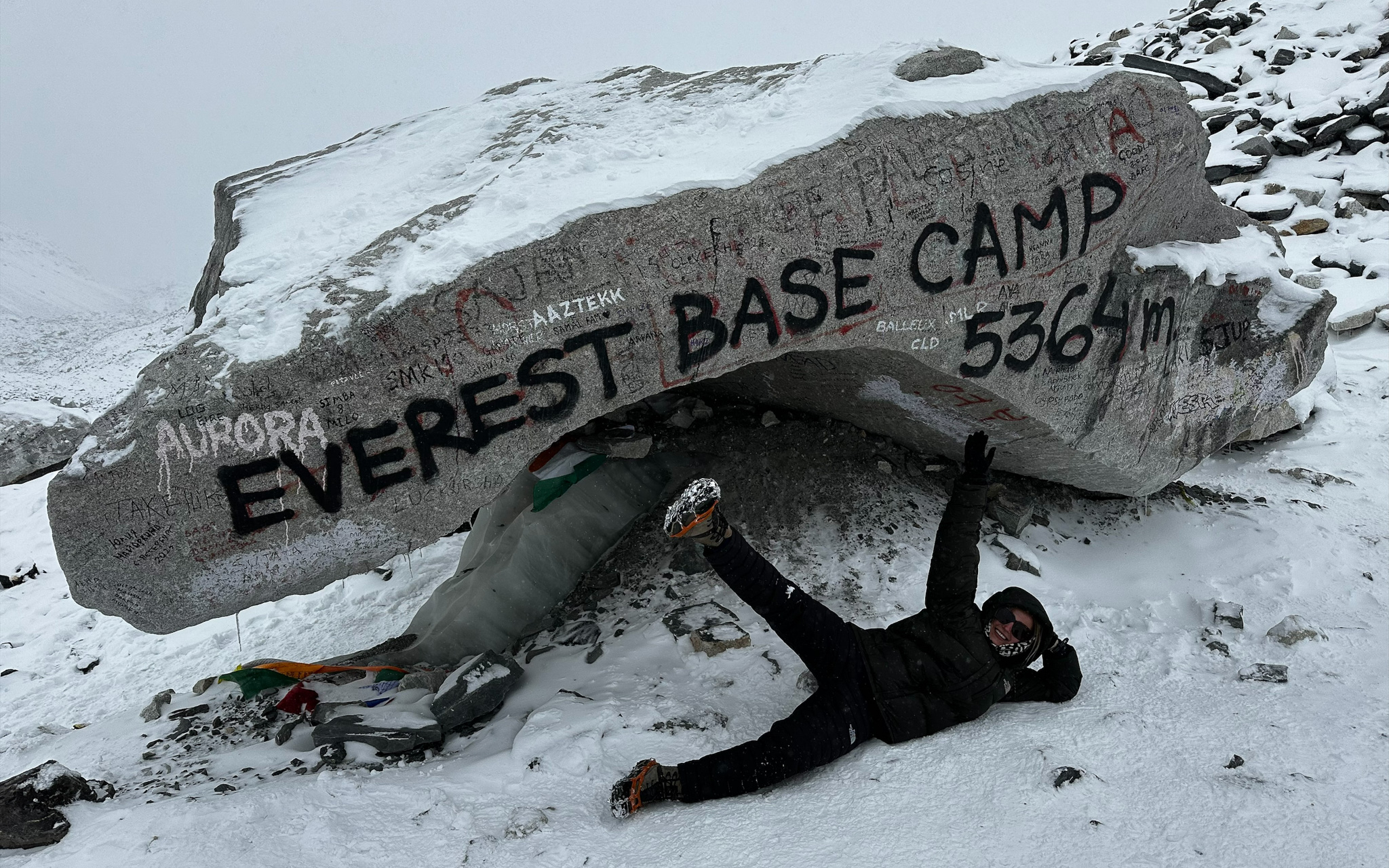 Hiker ligt vrolijk in de sneeuw voor de bekende rots bij Everest Base Camp op 5364 meter hoogte in Nepal.