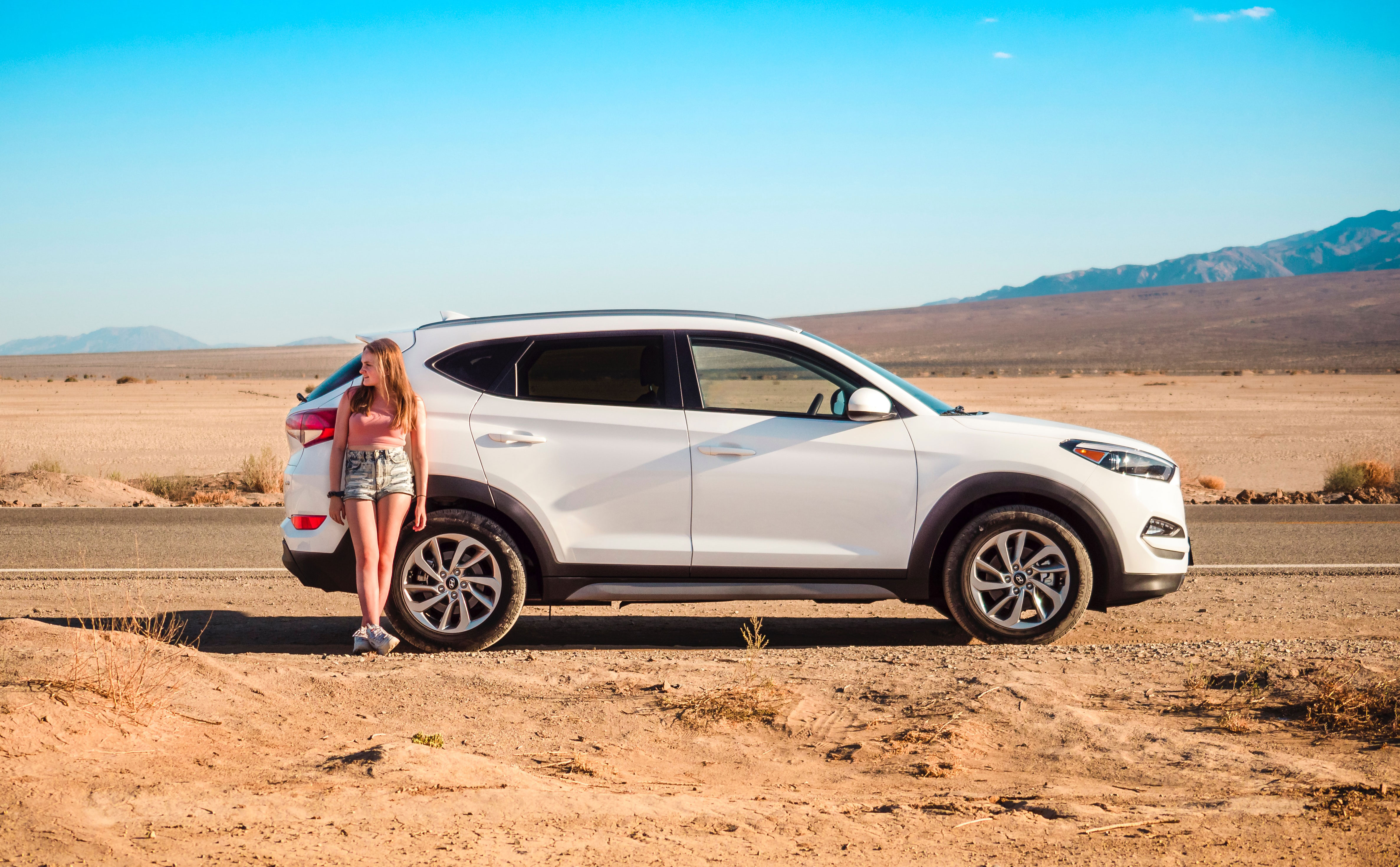 Een jonge vrouw leunend tegen haar huurauto in Death Valley in Californië, VS.