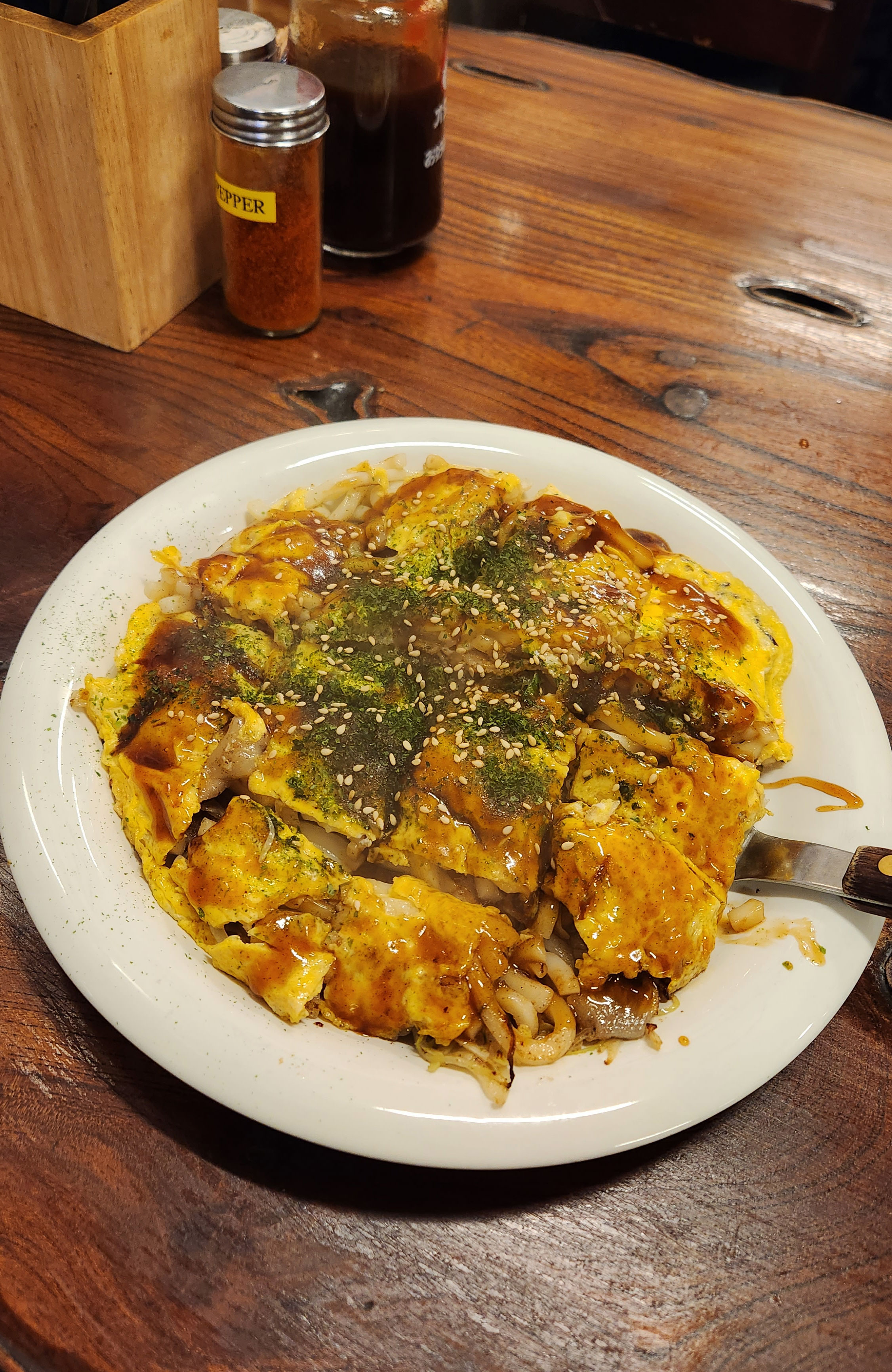 Gerecht okonomiyaki, een zoete pannekoek/omelet met noedels, groenten en saus.