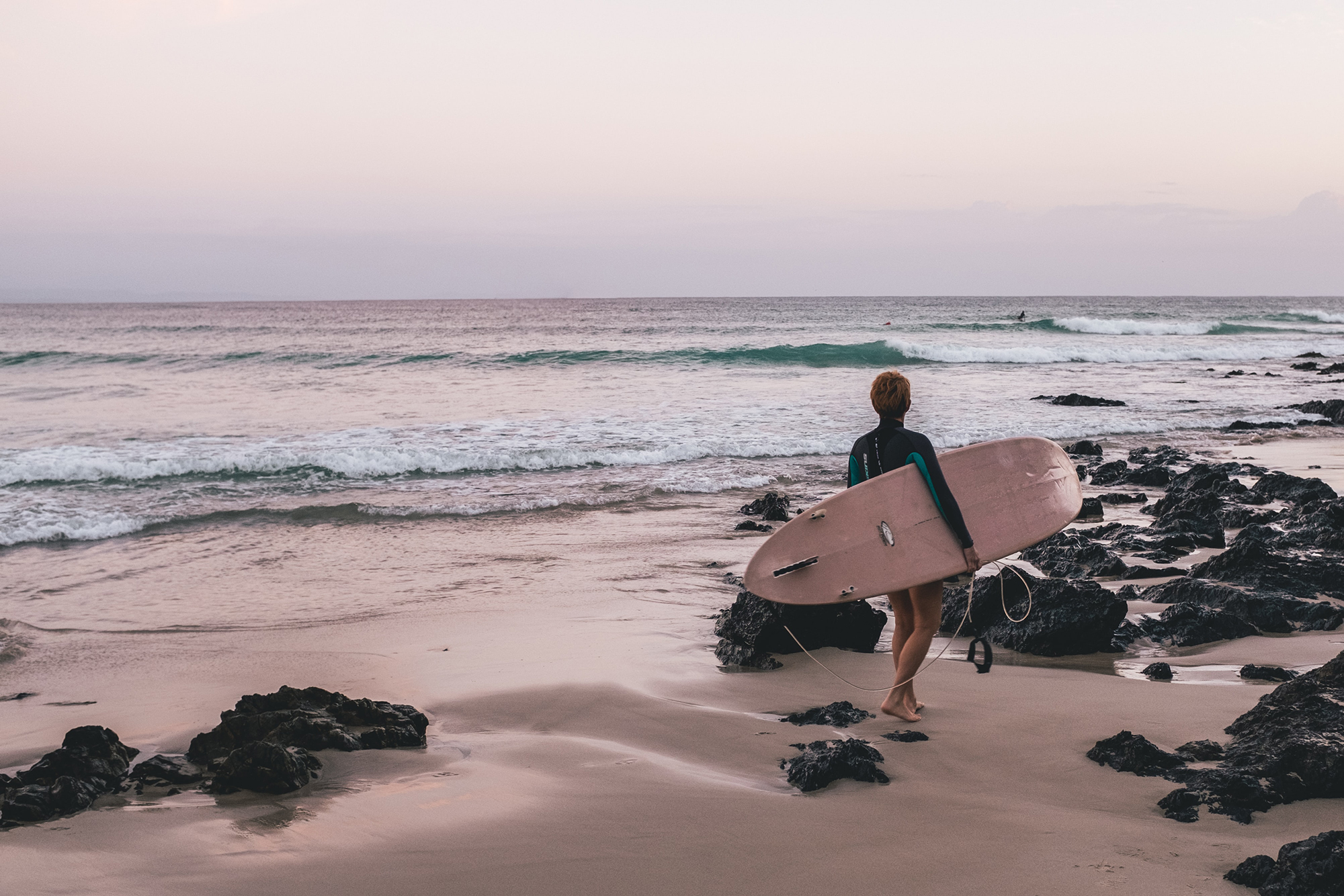 Iemand loopt op het strand met een surfboard onder zijn arm richting de zee