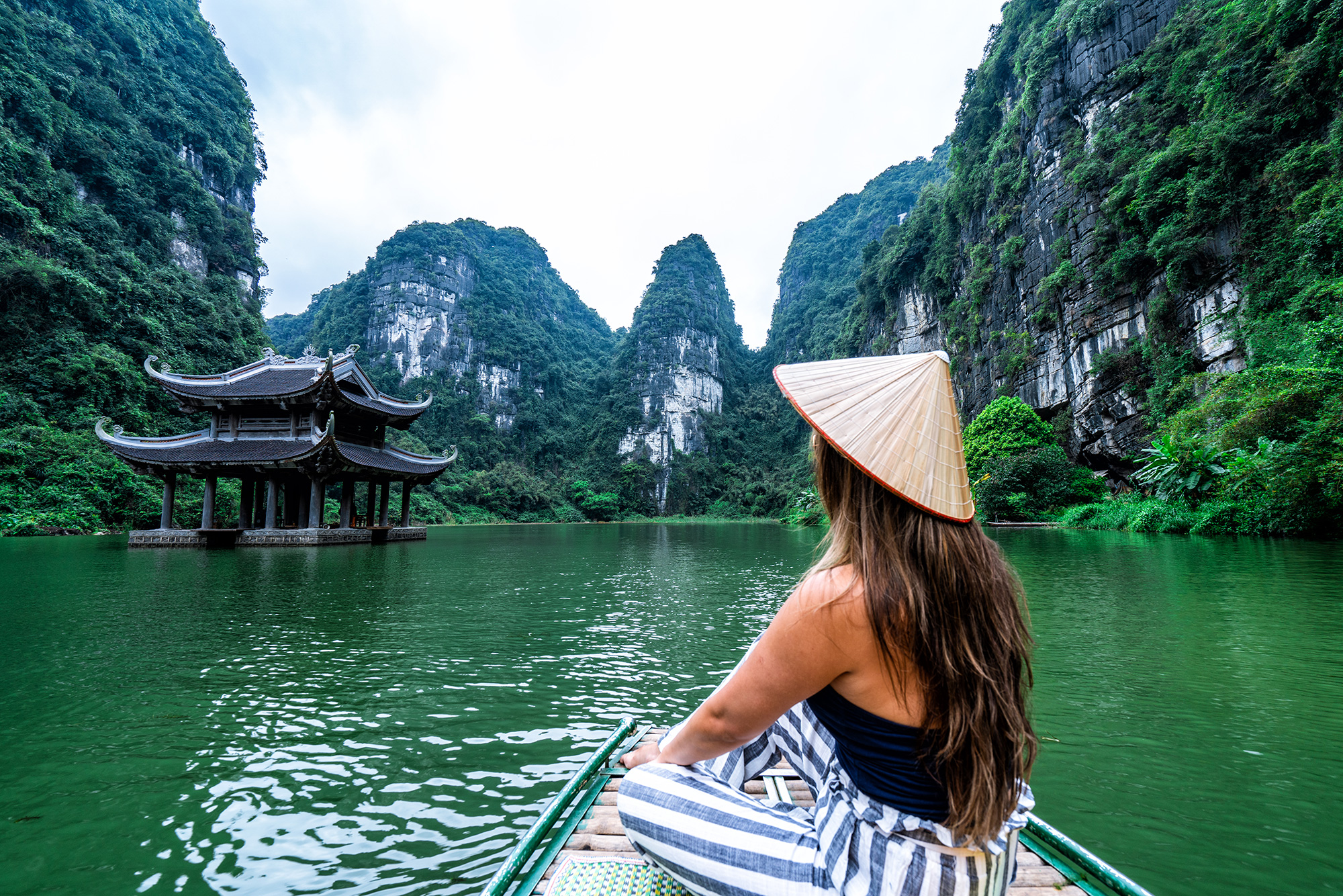 Toerist met traditionele hoed voor een meer tussen de bergen van Ninh Binh in Vietnam